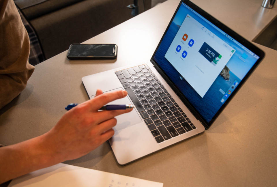 A laptop showing a website, with someone taking notes beside it